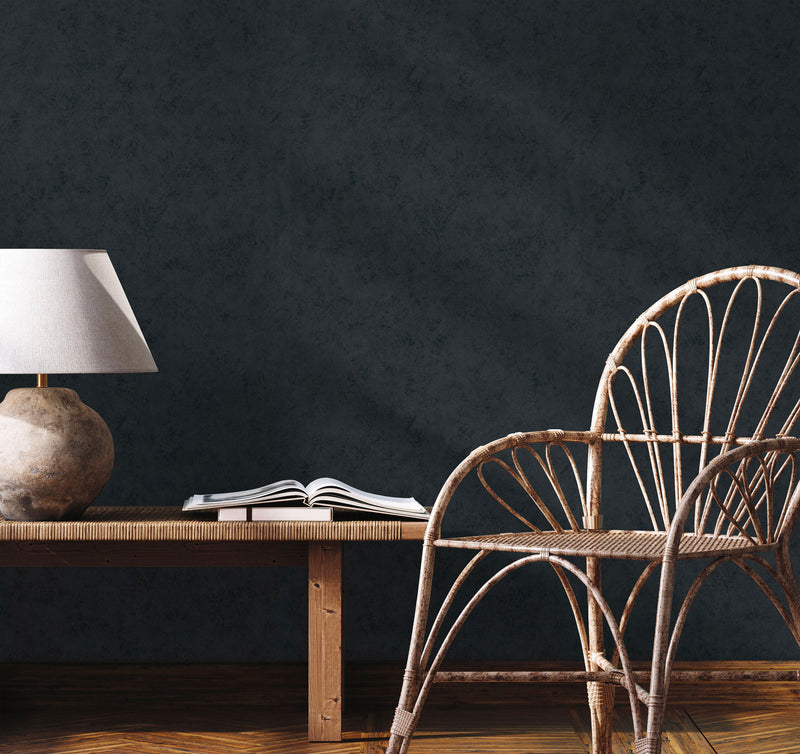 Parete antracite effetto intonaco Europarati collezione Friends con sedia in vimini e lampada da tavolo, stile minimal moderno