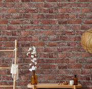 Parete decorata con carta da parati effetto mattoni rossi in un ambiente living con consolle in legno, rami di cotone in vaso e decorazioni in stile naturale/boho