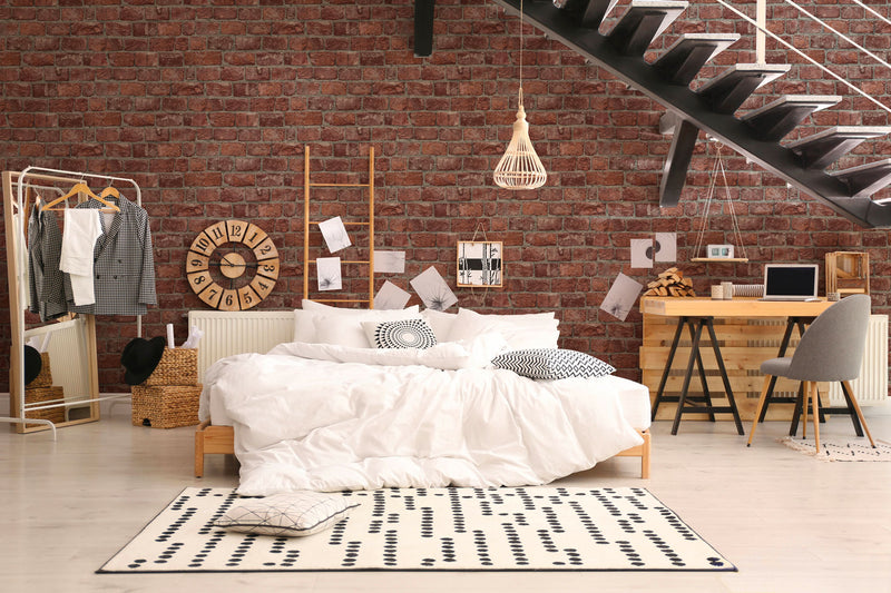 Camera da letto in stile loft industriale con grande parete in mattoni rossi Europarati FRIENDS, letto bianco, tappeto geometrico e scala moderna in metallo nero