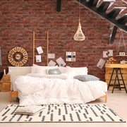 Camera da letto in stile loft industriale con grande parete in mattoni rossi Europarati FRIENDS, letto bianco, tappeto geometrico e scala moderna in metallo nero
