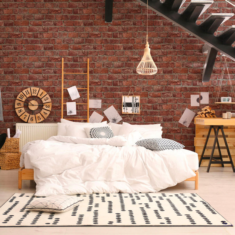 Camera da letto in stile loft industriale con grande parete in mattoni rossi Europarati FRIENDS, letto bianco, tappeto geometrico e scala moderna in metallo nero