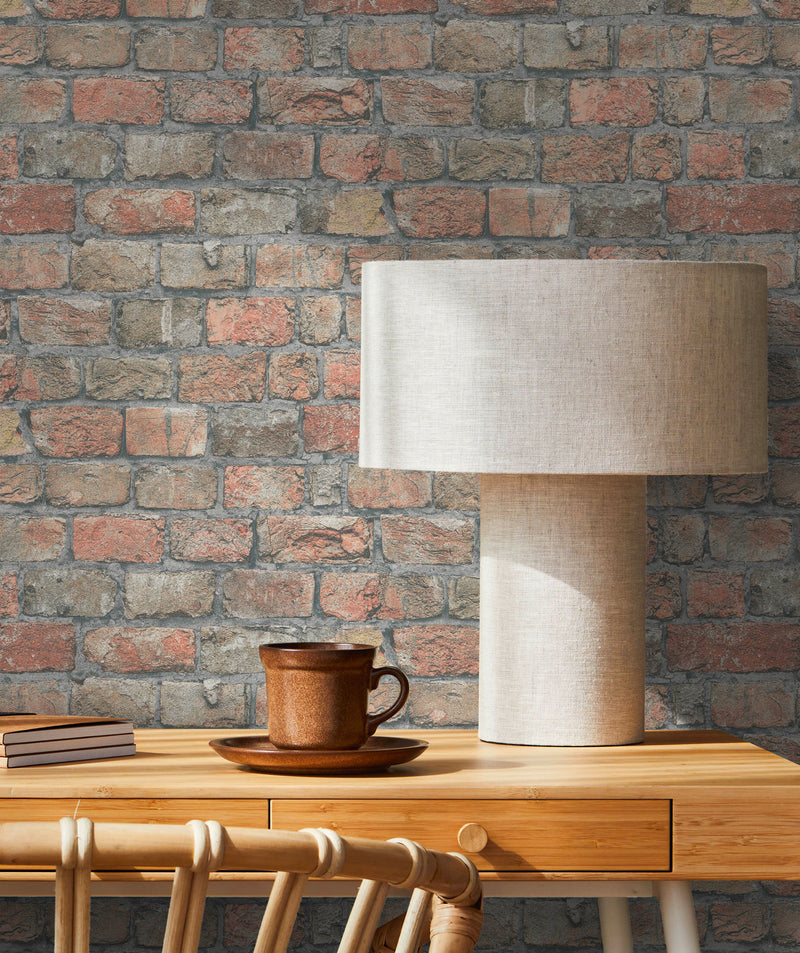 Dettaglio di una scrivania in legno con lampada di design e tazza di caffè su sfondo di carta da parati materica effetto mattoni recuperati
