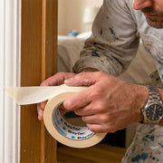 Imbianchino professionista che applica il nastro carta Bayfar 50mm su uno stipite in legno per proteggere le superfici durante la pittura