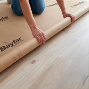 Dettaglio della posa del rotolo di cartone protettivo Bayfar sul pavimento in legno per coprire e proteggere la superficie durante la ristrutturazione.