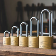 Una serie di cinque lucchetti Potent in ottone disposti in ordine crescente di dimensione su un banco da lavoro in legno rustico, con attrezzi da officina sfocati sullo sfondo