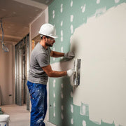 Un operaio specializzato con casco protettivo applica lo stucco rasante bianco su lastre di cartongesso verde idrorepellente